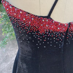 Puede incluir: Vestido de terciopelo negro con un escote de cuentas rojas y plateadas.