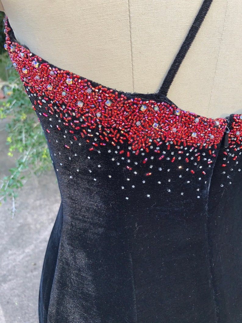 Puede incluir: Vestido de terciopelo negro con un escote de cuentas rojas y plateadas.