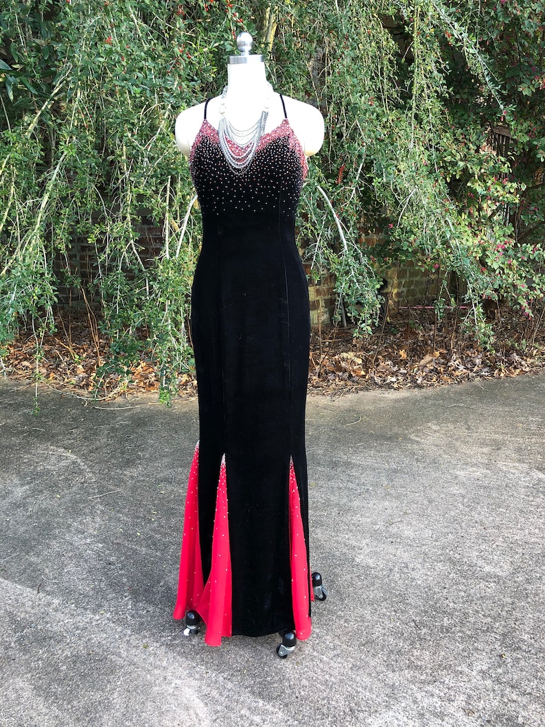 Puede incluir: Un vestido de noche de terciopelo negro con una superposici&oacute;n de gasa roja. El vestido presenta un corpi&ntilde;o con cuentas y una silueta ajustada.