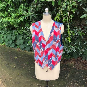 Può includere: Un gilet di patchwork rosso, bianco e blu con un motivo a chevron. Il gilet è realizzato in tessuto con un motivo a stelle e strisce. Il gilet è su un manichino bianco.