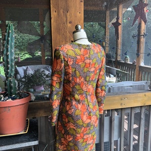 Peut inclure: Une robe vintage &agrave; motif floral dans les tons orange, vert et gris. La robe a des manches longues et une silhouette ajust&eacute;e.