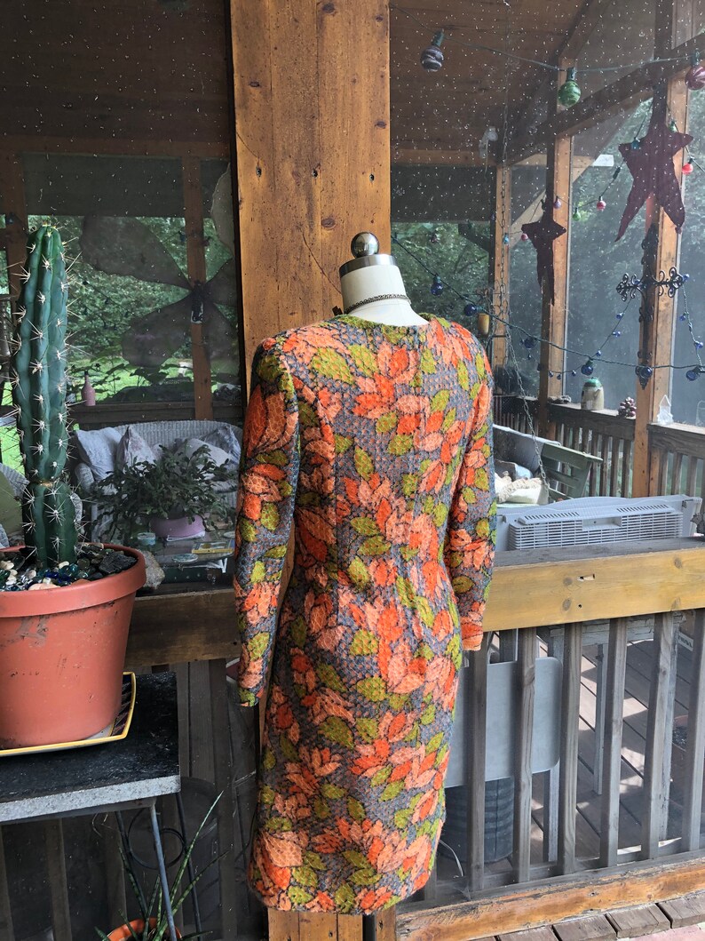 Peut inclure: Une robe vintage &agrave; motif floral dans les tons orange, vert et gris. La robe a des manches longues et une silhouette ajust&eacute;e.