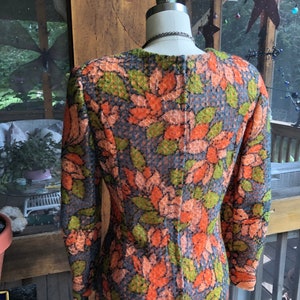 Peut inclure: Une robe &agrave; manches longues avec un motif floral dans les tons orange, vert et bleu. La robe a une silhouette ajust&eacute;e et un col rond.