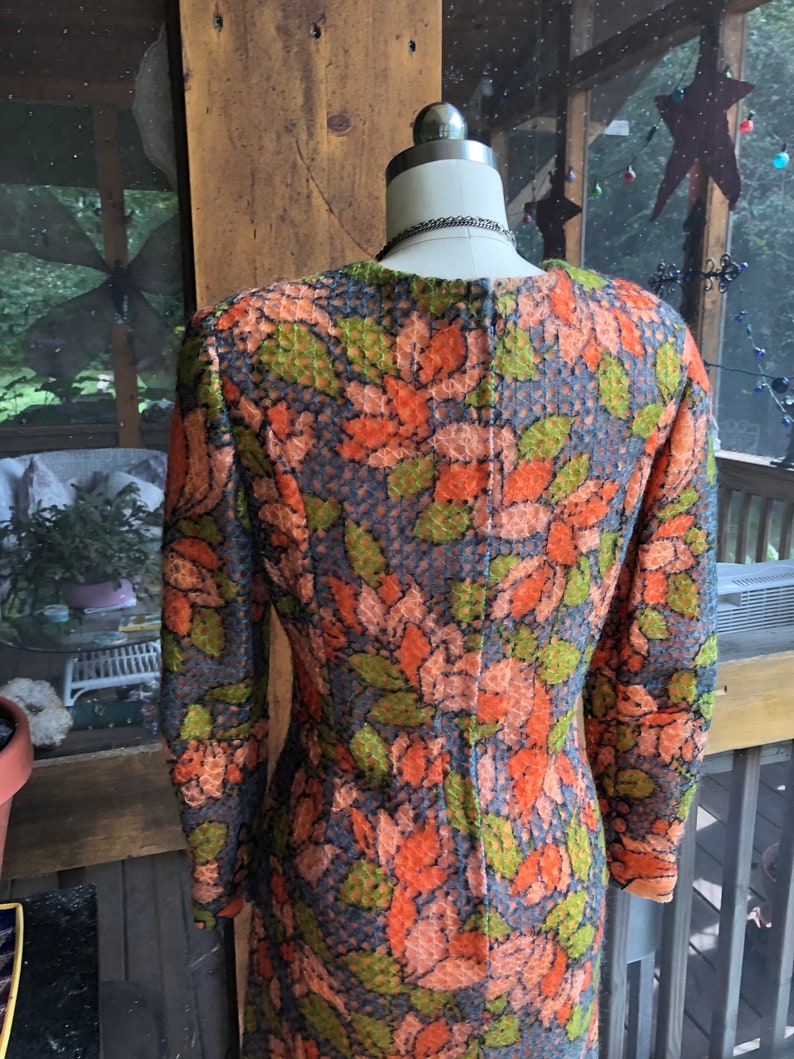Peut inclure: Une robe &agrave; manches longues avec un motif floral dans les tons orange, vert et bleu. La robe a une silhouette ajust&eacute;e et un col rond.