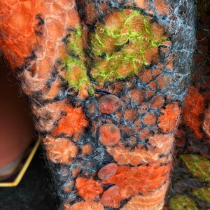Peut inclure: Gros plan d'un v&ecirc;tement tricot&eacute; avec une surface textur&eacute;e et duveteuse. Le v&ecirc;tement est orange, vert et noir avec un motif en filet noir. Il y a quatre gros boutons ronds orange sur le v&ecirc;tement.