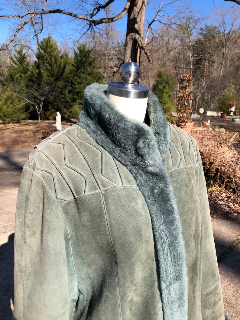 May include: A green suede jacket with a faux fur collar and lining. The jacket has a quilted design on the shoulders and a zipper closure.
