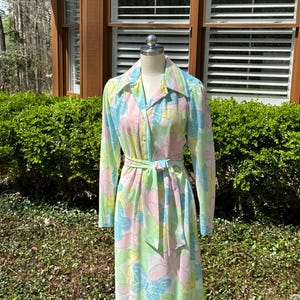 Pode incluir: Um vestido branco de manga comprida com estampa de borboletas coloridas. O vestido tem um cinto de laço e uma gola.