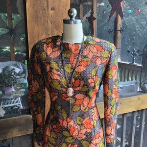 Peut inclure: Une robe vintage &agrave; motif floral dans les tons orange, vert et bleu. La robe a des manches longues et une silhouette ajust&eacute;e. Elle est expos&eacute;e sur un mannequin.