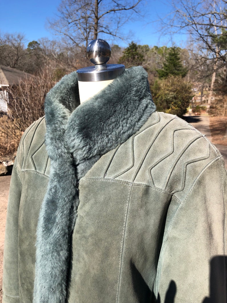 May include: A green suede jacket with a shearling collar. The jacket has a zipper closure and a quilted design on the shoulders.