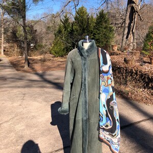 May include: A long, green suede coat with a fur collar and cuffs. The coat is on a mannequin and has a patterned scarf draped over it.