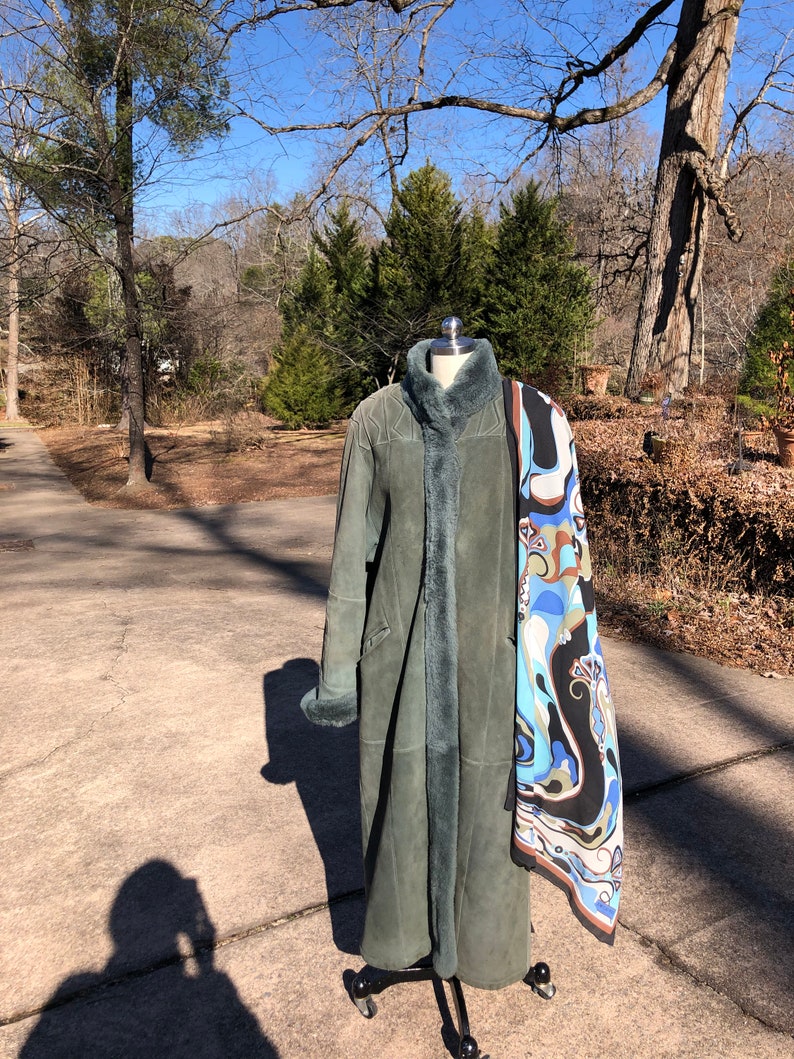 May include: A long, green suede coat with a fur collar and cuffs. The coat is on a mannequin and has a patterned scarf draped over it.