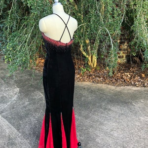 Puede incluir: Un vestido de noche de terciopelo negro con falda de sat&eacute;n rojo. El vestido tiene una espalda con tirantes cruzados y est&aacute; adornado con pedrer&iacute;a.