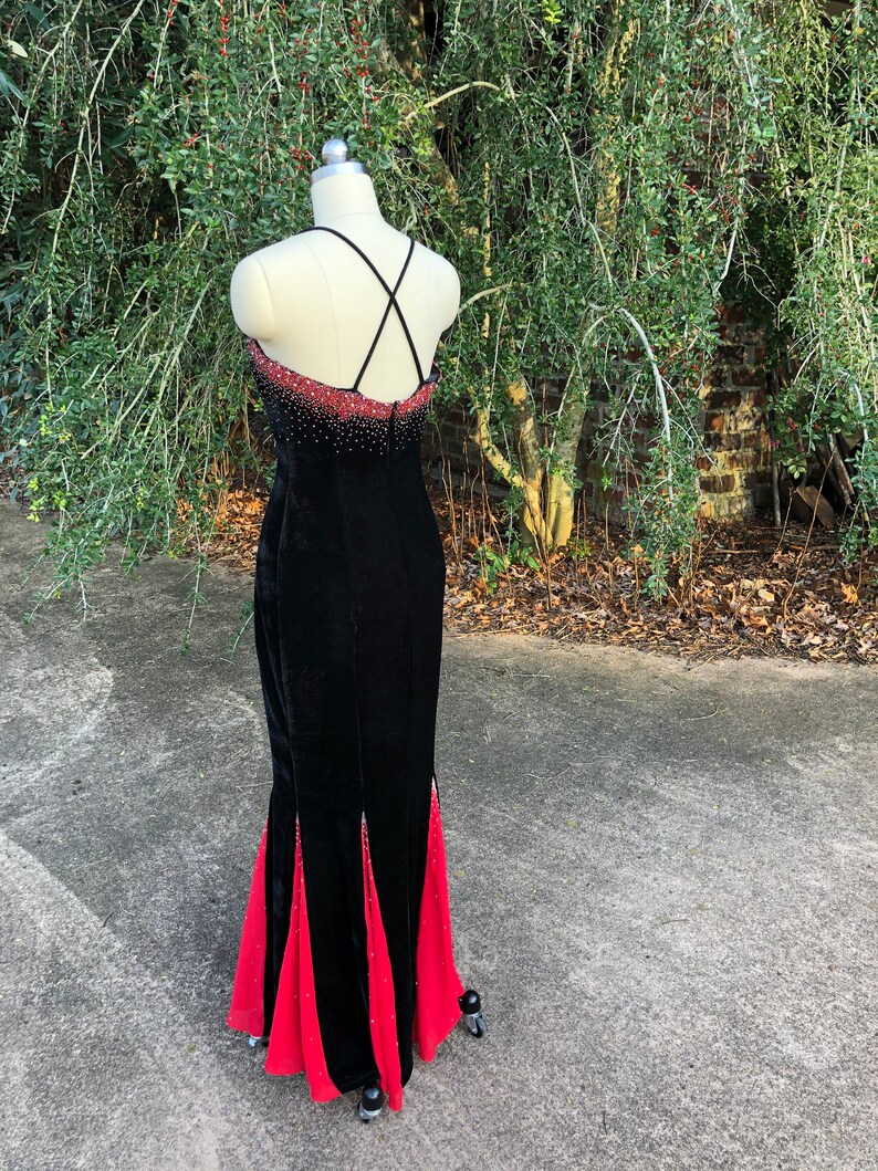 Puede incluir: Un vestido de noche de terciopelo negro con falda de sat&eacute;n rojo. El vestido tiene una espalda con tirantes cruzados y est&aacute; adornado con pedrer&iacute;a.