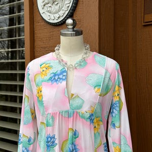 Puede incluir: Un vestido rosa de manga larga con escote en V y estampado floral de flores azules y amarillas. El vestido tiene una cintura fruncida y mangas largas.