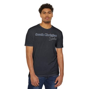 May include: Dark gray t-shirt with the text "South Christian Sailors" in white and blue. The shirt is a crew neck style and is paired with blue jeans. The overall look is casual and comfortable.