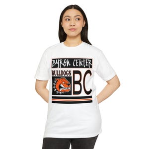 May include: White t-shirt featuring the text "BYRON CENTER BULLDOGS" in black and orange. The shirt includes a graphic of a bulldog head and the letters "BC". The design is centered on the front of the shirt.