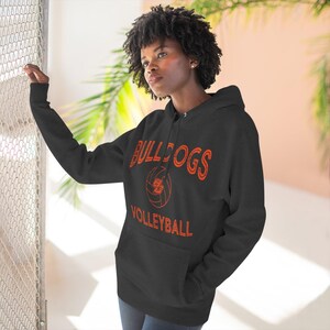 May include: Black hoodie featuring the word "BULLDOGS" in orange, above a volleyball graphic, and the word "VOLLEYBALL" below. The hoodie has a front pocket and a drawstring hood.