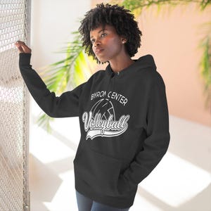 May include: Black hoodie with a kangaroo pocket and a drawstring hood. The front displays the text "BYRON CENTER Volleyball" in white, with a volleyball graphic. The sweatshirt is worn by a person.