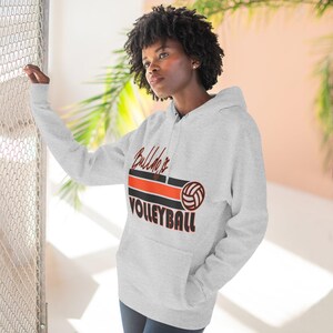 May include: A pale grey hoodie with a front pocket and a drawstring hood. The hoodie displays the text "Bulldogs Volleyball" in black and orange, accompanied by a volleyball graphic. The design is centered on the chest.