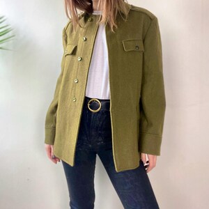 May include: A green utility jacket with a button-up front and two flap pockets. The jacket has a collar and long sleeves.