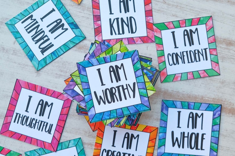Op de afbeelding: Een stapel kleurrijke affirmatiekaarten met de zin "Ik ben" en een positieve affirmatie op elke kaart. De kaarten hebben een glas-in-loodontwerp met een witte rand.