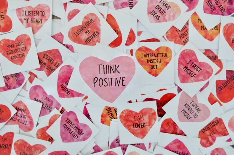 May include: A collection of pink and red heart-shaped stickers with positive affirmations printed on them. The stickers have watercolor-like designs and include phrases like "Think Positive", "I Love Myself Completely", and "I Trust Myself".