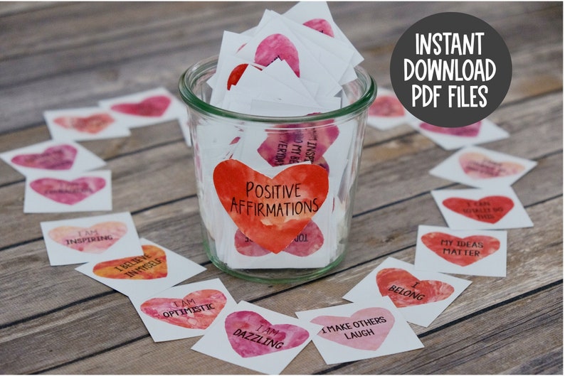 May include: A glass jar filled with small white cards with positive affirmations printed on them in the shape of hearts. The jar is labeled "Positive Affirmations".