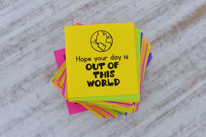 May include: A stack of colorful sticky notes with a yellow note on top that says "Hope your day is OUT OF THIS WORLD" with a black and white drawing of a globe.