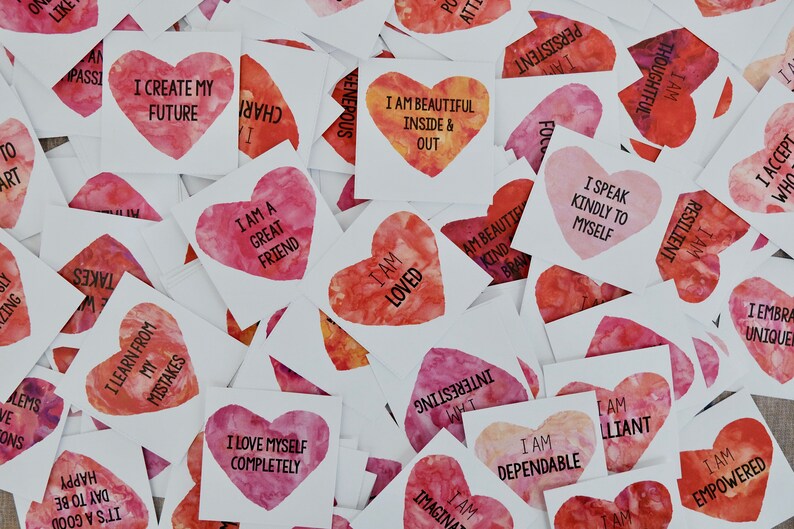 May include: A collection of pink and red heart-shaped affirmation cards with watercolor designs. The cards feature positive messages such as "I am loved", "I am beautiful inside and out", and "I create my future".