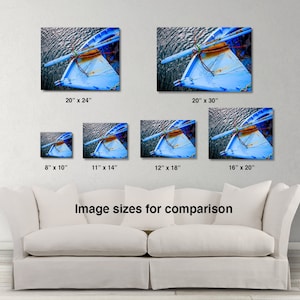 May include: A close-up of a blue wooden boat with a rope tied to the bow. The boat is floating in the water and the surface of the water is visible in the background. The image is a comparison of different sizes for a print.