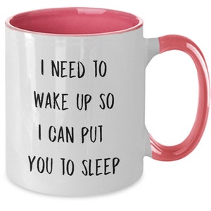 May include: White coffee mug with a pink rim and handle. The mug has black text that reads "I need to wake up so I can put you to sleep."