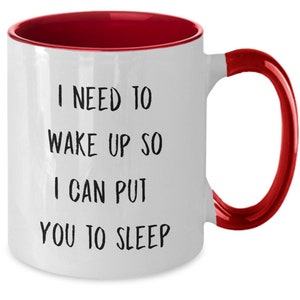 May include: White ceramic coffee mug with a red rim and handle. The mug has black text that reads "I need to wake up so I can put you to sleep."
