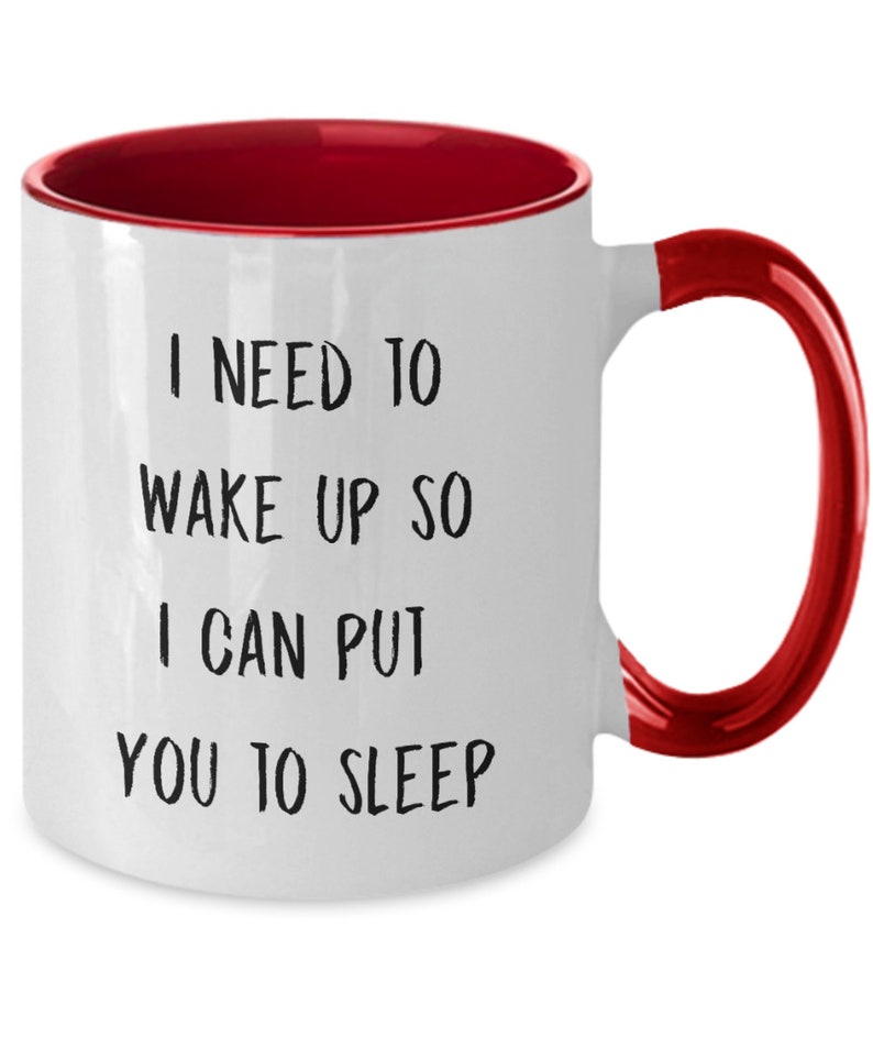 May include: White ceramic coffee mug with a red rim and handle. The mug has black text that reads "I need to wake up so I can put you to sleep."