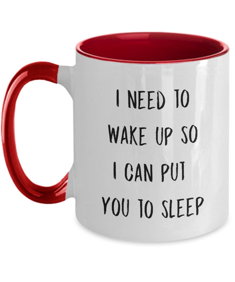 May include: White ceramic coffee mug with a red rim and handle. The mug has black text that reads "I need to wake up so I can put you to sleep."