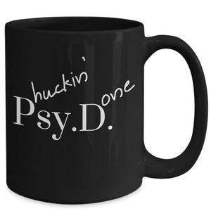 May include: Black ceramic coffee mug with white text that reads "Huckin' one Psy.D."