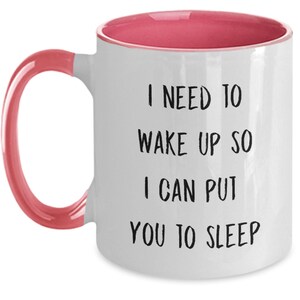 May include: White ceramic coffee mug with a pink rim and handle. The mug has black text that reads "I need to wake up so I can put you to sleep."