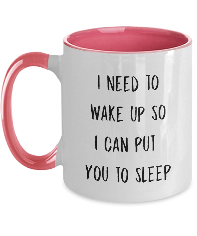 May include: White ceramic coffee mug with a pink rim and handle. The mug has black text that reads "I need to wake up so I can put you to sleep."