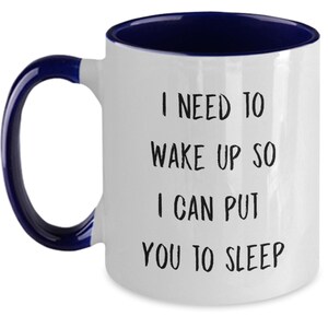 May include: White ceramic coffee mug with a blue rim and handle. The mug has black text that reads "I need to wake up so I can put you to sleep."