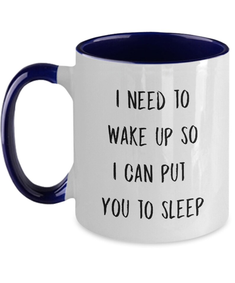 May include: White ceramic coffee mug with a blue rim and handle. The mug has black text that reads "I need to wake up so I can put you to sleep."