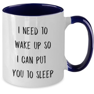 May include: White ceramic coffee mug with a blue rim and handle. The mug has black text that reads "I need to wake up so I can put you to sleep."