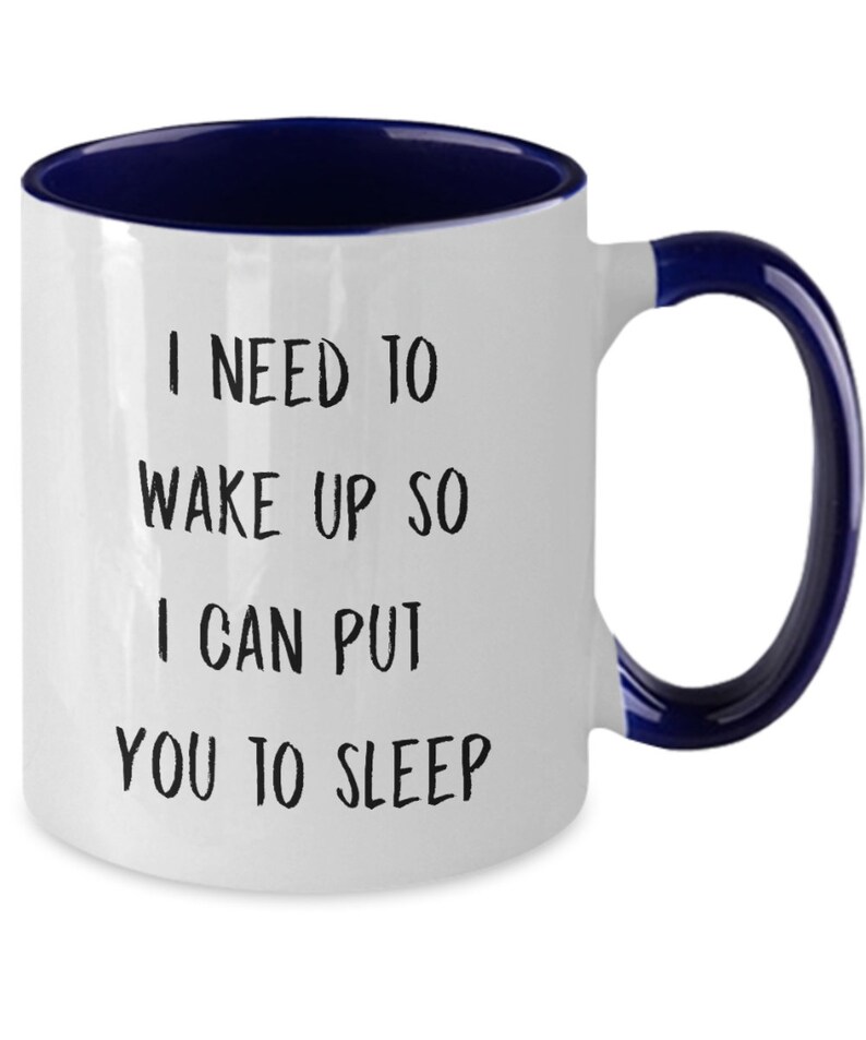 May include: White ceramic coffee mug with a blue rim and handle. The mug has black text that reads "I need to wake up so I can put you to sleep."