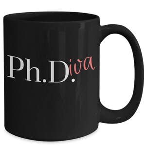 Peut inclure: Une tasse à café en céramique noire avec du texte blanc qui dit "Ph.D.iva" avec le mot "diva" en rose.