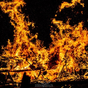 May include: A large bonfire with bright orange and yellow flames burning intensely. The flames are rising high into the air, creating a dramatic and powerful image.