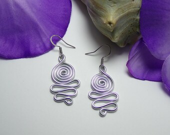 Puede incluir: Un par de pendientes de alambre plateado con un diseño en espiral. Los pendientes cuelgan de un gancho.