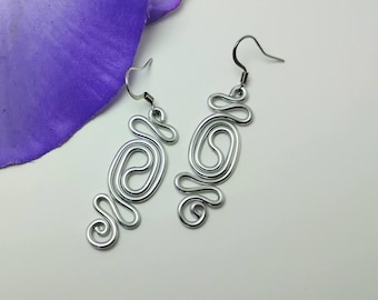 Puede incluir: Un par de pendientes de plata con un diseño abstracto único. Los pendientes están hechos de alambre retorcido y tienen un cierre de gancho.