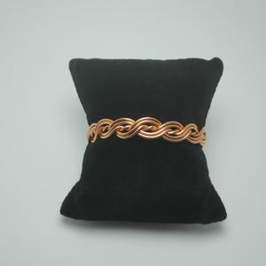 May include: A gold-toned braided wire bracelet on a black velvet cushion.