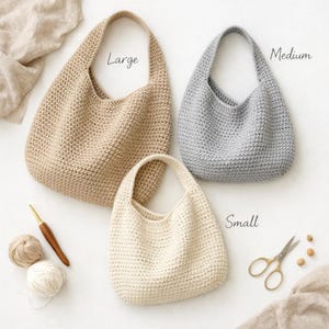 Puede incluir: Tres bolsos de ganchillo hechos a mano en diferentes tamaños: grande, mediano y pequeño. El bolso grande es beige, el mediano es gris y el pequeño es blanquecino. Los bolsos tienen forma redondeada con un asa. También se ven un ganchillo, hilo y tijeras.