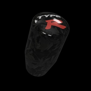 May include: A black carbon fiber shift knob with the text "TYPE R" in white and a red "R" logo. The knob has a glossy finish and a textured pattern. The background is black.