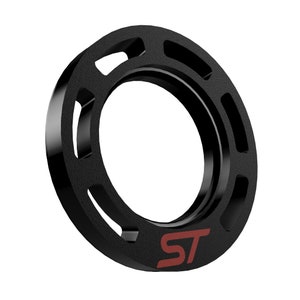 Può includere: Un oggetto circolare nero con una superficie strutturata e un'apertura centrale. L'oggetto presenta diverse sezioni ritagliate attorno al suo perimetro. Le lettere "ST" sono stampate in rosso sulla superficie.