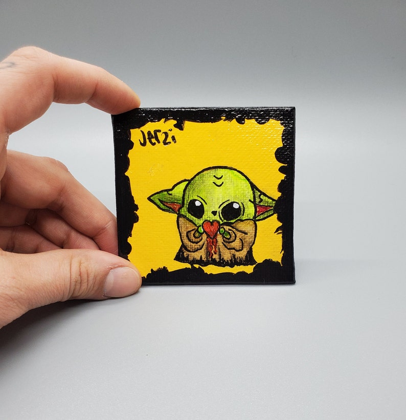 May include: A hand-painted canvas featuring a green cartoon character holding a red heart. The character has large eyes and is wearing a brown outfit. The canvas has a black border and the text "JATZI" in black.